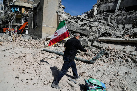 A man carries an Iranian flag to place on the rubble