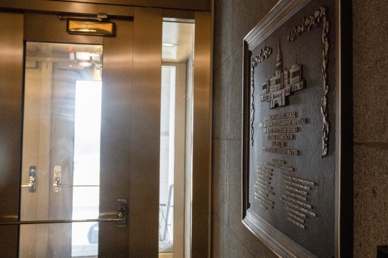 A metal plaque on a stone interior wall near a glass doorway at the Capitol