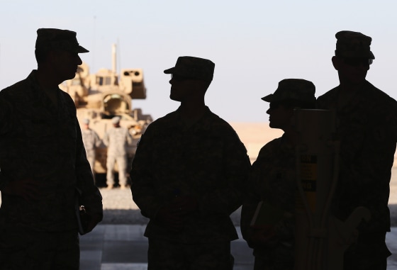 Four soldiers are silhouetted by bright desert sunlight.