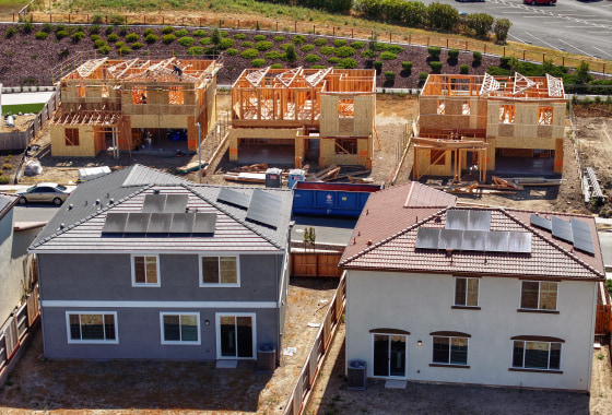 Three partially-built houses stand behind two finished houses with solar panels.