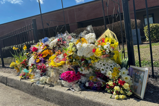 A pile of bouquets resting on a curb in front of a red brick building