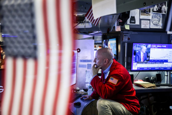 A person sits at a work desk with various monitors, an American flag covers half of the photo in the foreground