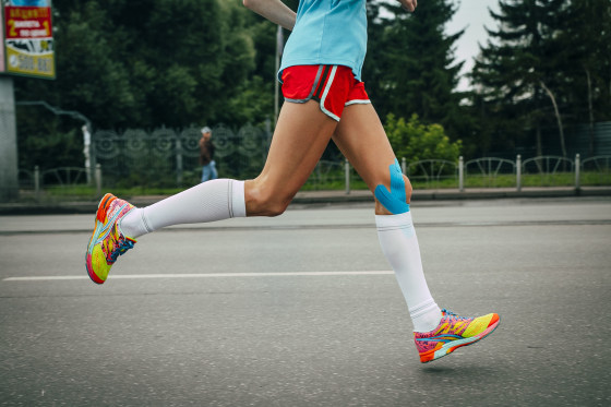 Image: A girl athlete running with her knees in blue kinesiology taping