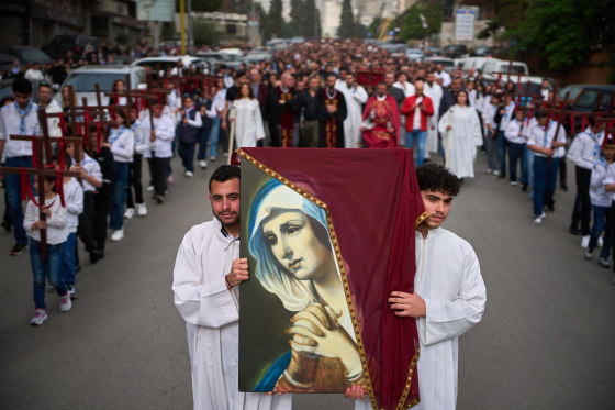 Parishioners walk in a procession outside, two people in white robes hold a painted picture of Mother Mary