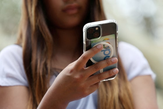 A teenager poses holding a mobile phone as law banning social media for users under 16 in Australia takes effect, in Sydney