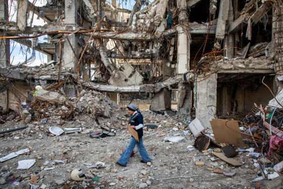 A woman walks amid rubble while holding a sign
