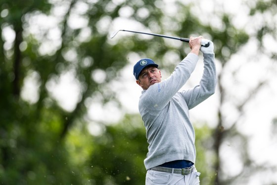 Bryson DeChambeau holds his golf club in the air after playing a stroke outside