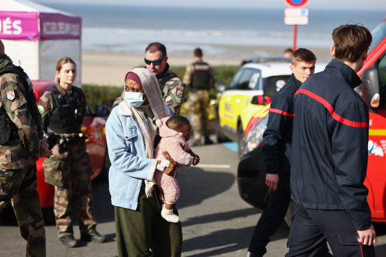 A woman with a baby stands next to rescue units after an attempt to cross the English Channel