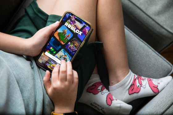 A child holds a smartphone displaying the Roblox app login page