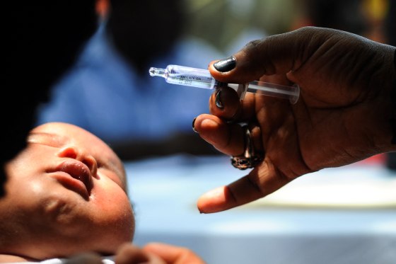 A hand holds a vaccine administer near a infant's face