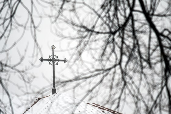 A cross sits atop a building at the Archdiocese of Denver, shrouded by branches