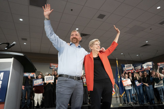 Elizabeth Warren and Graham Platner wave with their arms over each other's shoulders during a campaign event.