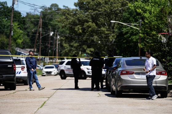 Yellow police tape stretched in front of law enforcement officials in a residential street.