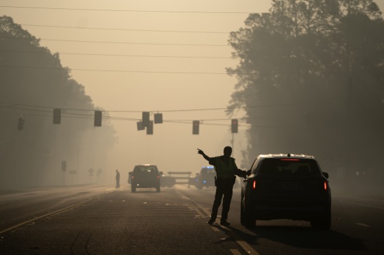 A police officer points a car away from an intersection under hazy, smoky skies.