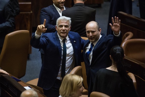 Naftali Bennett and Yair Lapid stand with their arms around each other's backs on the floor of the Israeli parliament.