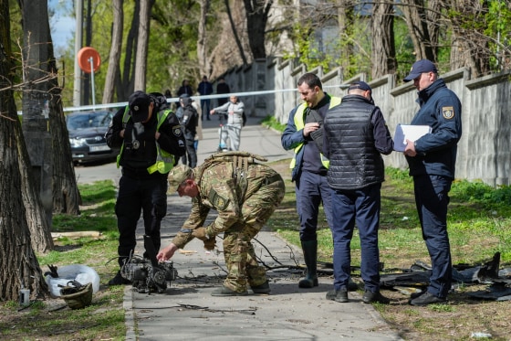 Police officers inspect fragments of a Russian drone on a sidewalk outside
