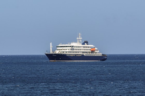 A blue and white cruise ship floats in calm waters under a clear blue sky.