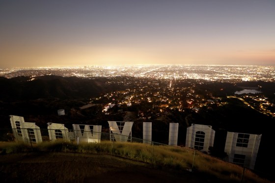 The back side of the HOLLYWOOD sign in Los Angeles stands in front of the city skyline at dusk.
