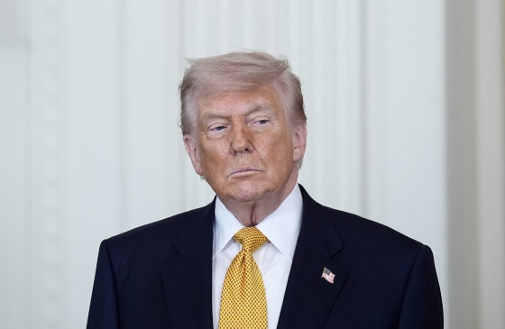 Donald Trump gazes to the side while standing in front of a white wall in the White House.