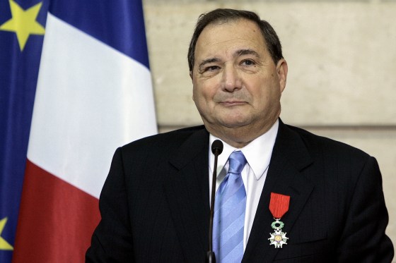 Abe Foxman standing at a microphone wearing a red ribboned medal on his lapel.