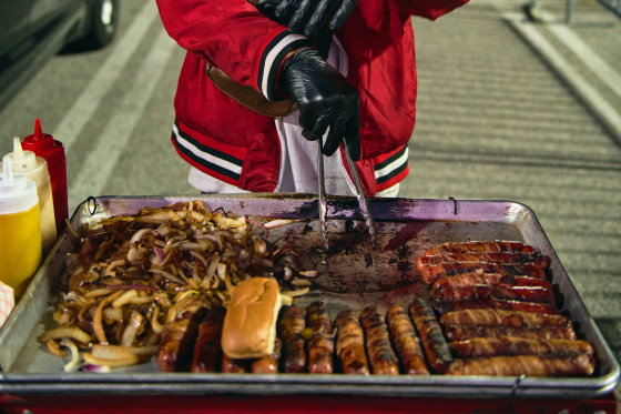 Henrry Josue uses tongs to grab hotdogs on a tray outside