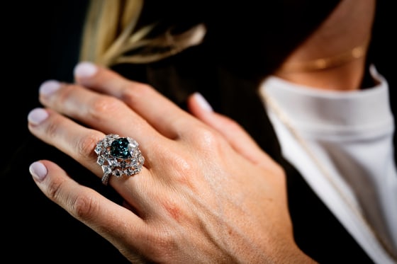 A large blue-green diamond rin on a person's hand seen in a close-up view.
