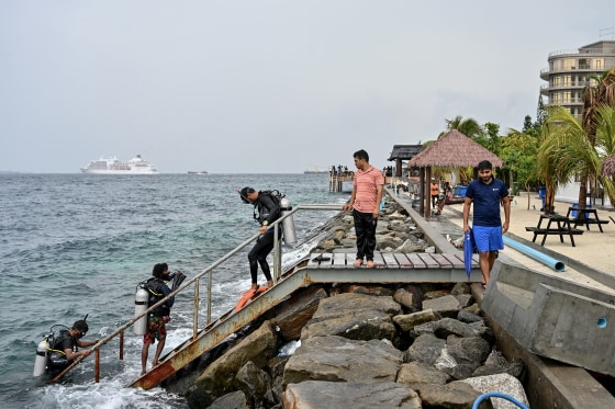 Three men wearing diving equipment make their way up a staircase from the water. 