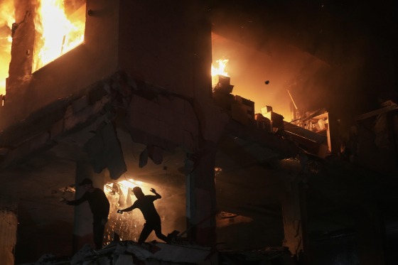A person silhouetted by the flames of a burning building at night.