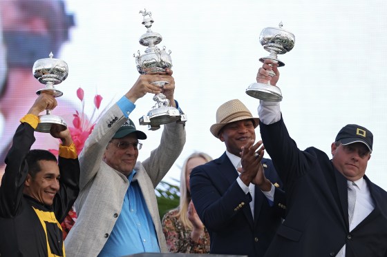 Three men smile while holding silver trophies high into the air.