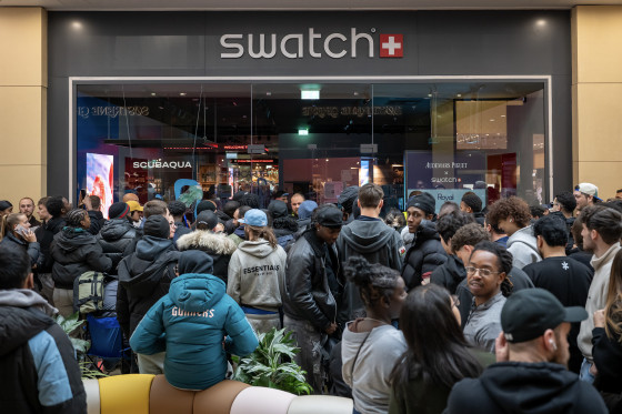 Dozens of young adults dressed in dark jackets congregate outside a Swatch retail store in a shopping mall.