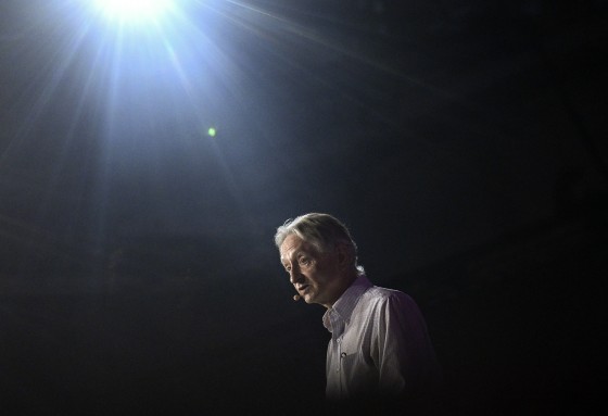 Geoffrey Hinton speaks using a wireless lav mic. He is lit by an overhead spotlight.