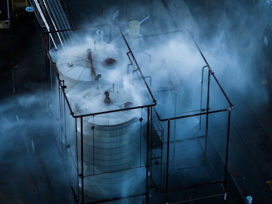 Spraying water and mist on a large chemical tank at dusk.