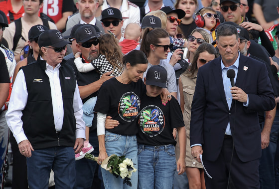 A somber grouping of people at a racetrack wearing black caps with the number 8 on them.