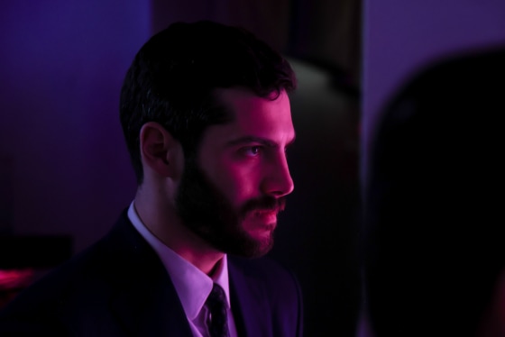 Alex Bores stands in a dimly lit room with purple and magenta colored lighting.