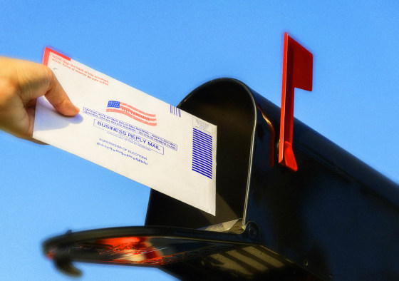 Woman's hand placing a mail-in election ballot in a mailbox against a blue sky