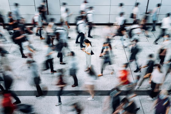 Image: Young woman using smartphone surrounded by commuters rushing by in subway station