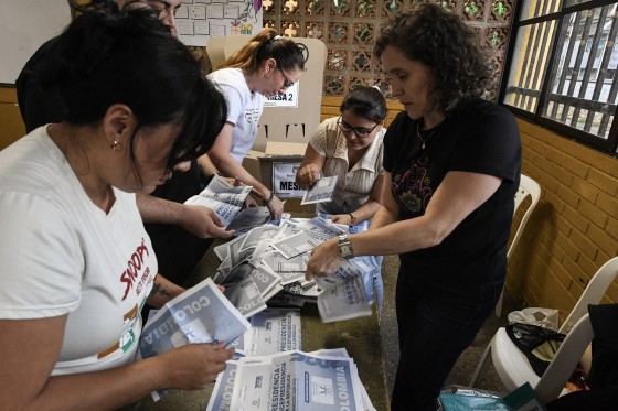 Five election officials sorting paper ballots on a folding table.