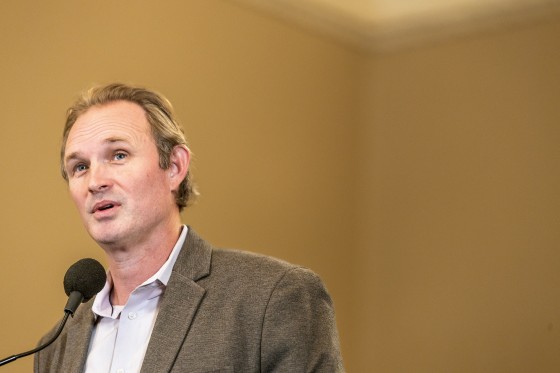James Gallagher speaking into a microphone at the left of the frame.