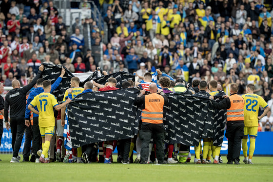 Players and security officials holding up a black banner on the soccer field.