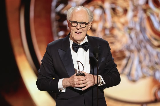 John Lithgow holding an Emmy, dressed in a tuxedo.