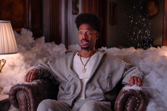 Marlon Wayans sits on a couch in a living room surrounded by foam with tears streaming down his face