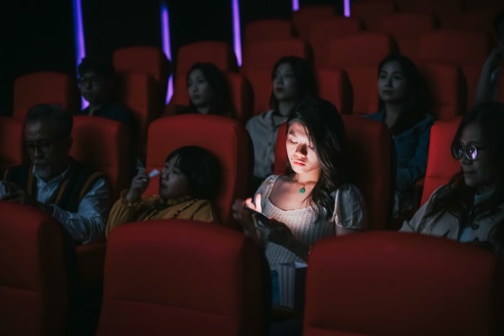 woman reading phone message during cinema movie show time in the dark ignoring and disturbing other audience around her