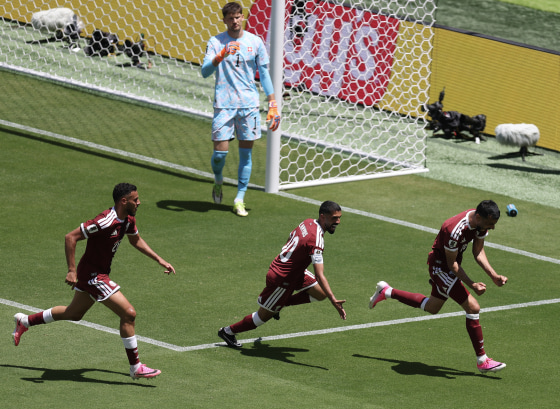 Three Qatari soccer players celebrating on the field in front of a goalie.