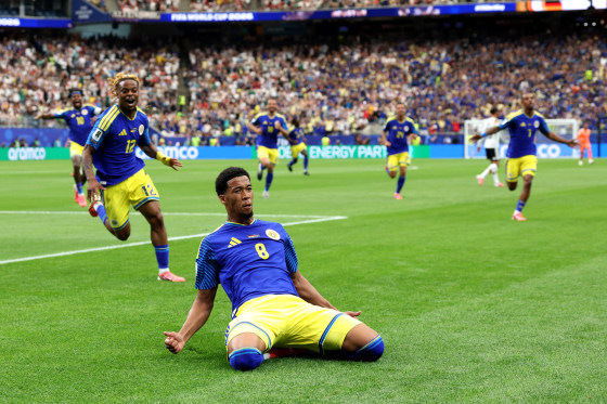 Livano Comenencia slides on his knees on the ground of the soccer field in celebration as his teammates run behind him
