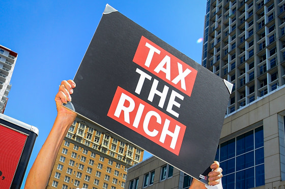 A person holds a sign that reads "TAX THE RICH."