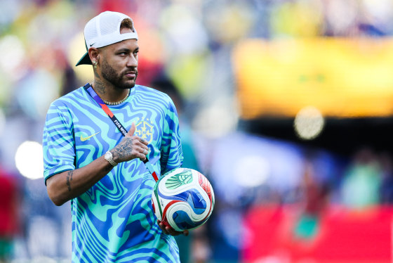 Neymar walks on the soccer field holding a soccer ball