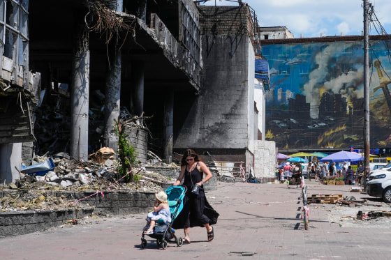 A mother pushes a stroller past a damaged building.