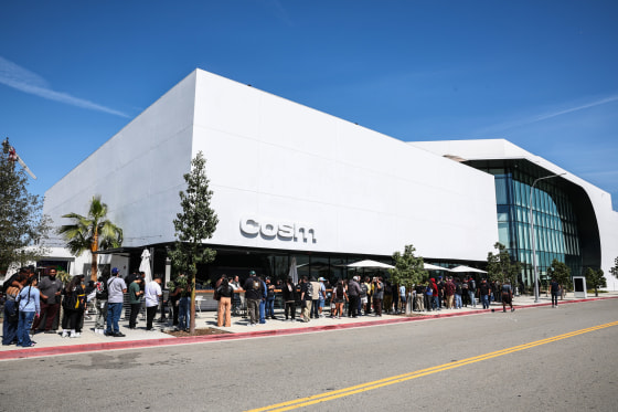 The exterior of Cosm Los Angeles, a white building facade, people in line wait to enter the building on the sidewalk