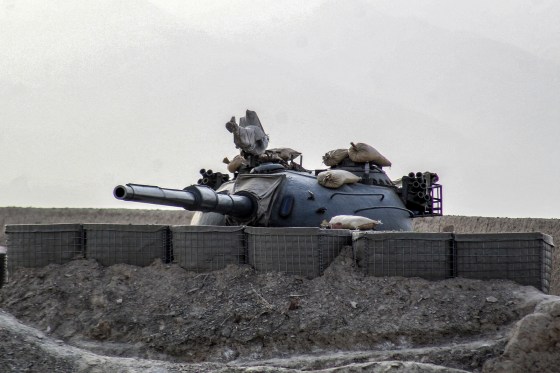 A military tank nestled behind blast walls on rocky soil.