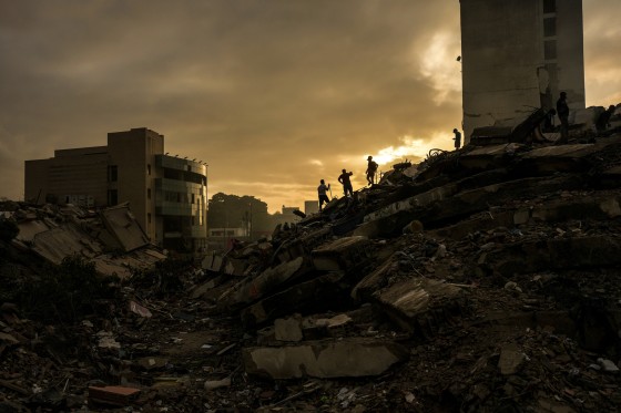 Men searching for survivors stand atop a mountain of rubble three days after twin earthquakes struck, in La Guaira.